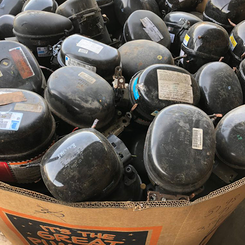 Black AC fridge compressors scrap metal with brand stickers in a big brown carton.